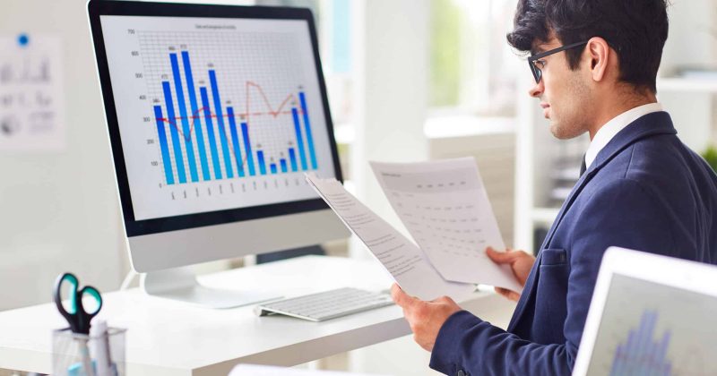 Businessman looking through papers by workplace and analyzing statistics